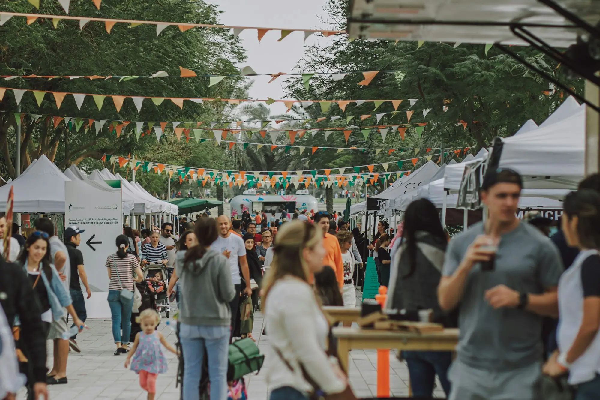 Crowds and food stalls under festoon bunting at an outdoor summer market