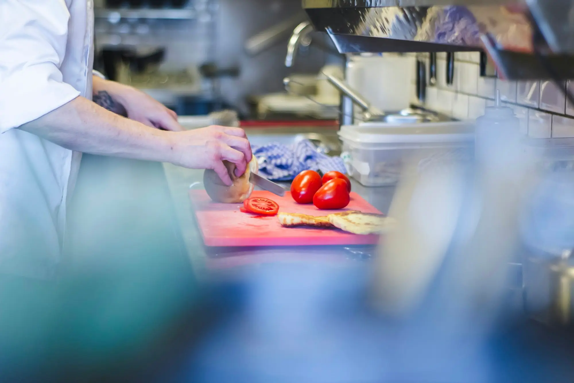 Food handler in gloves slicing fresh tomatoes in a commercial kitchen