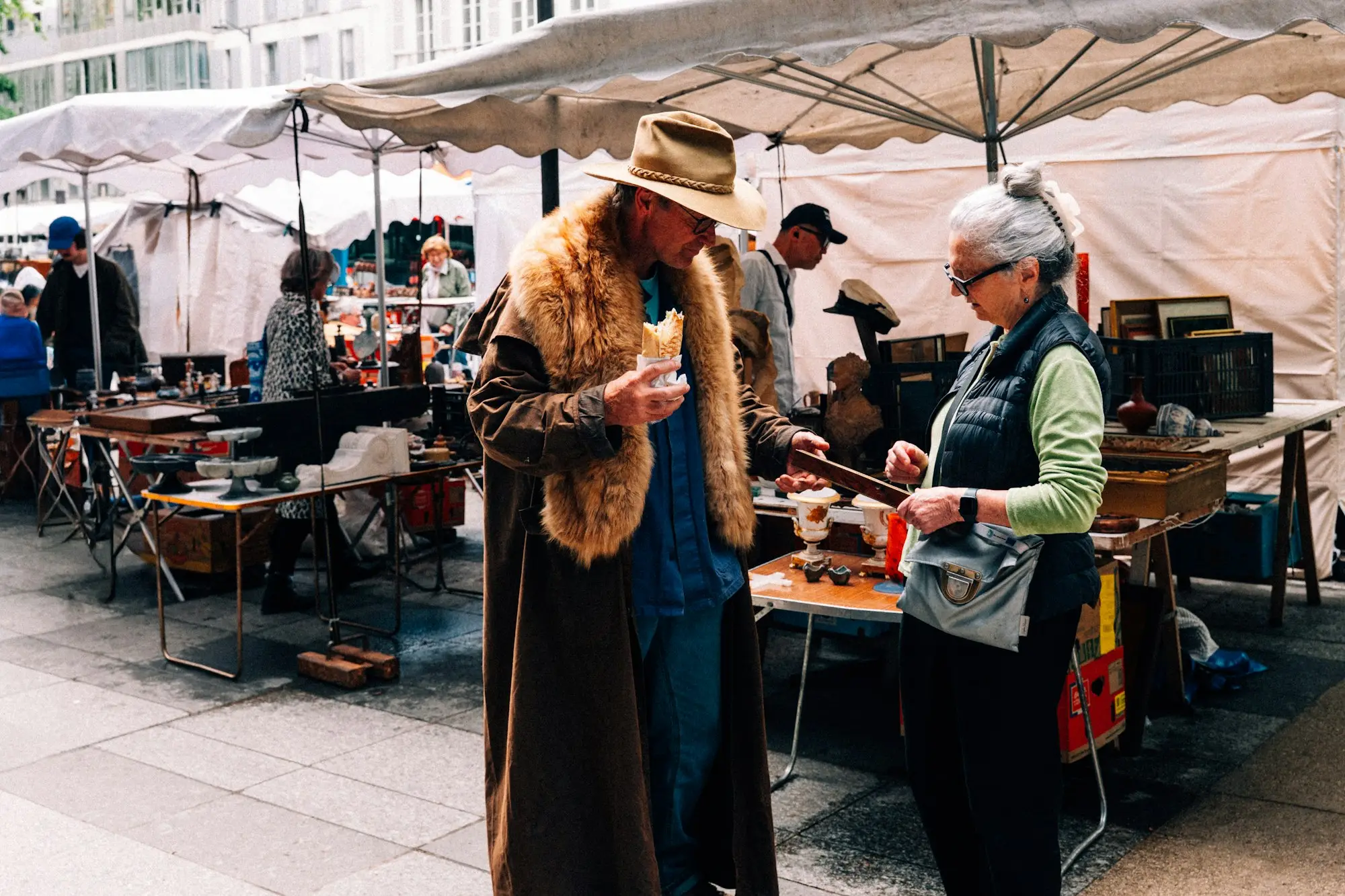 Shoppers browsing a market stall under white umbrellas