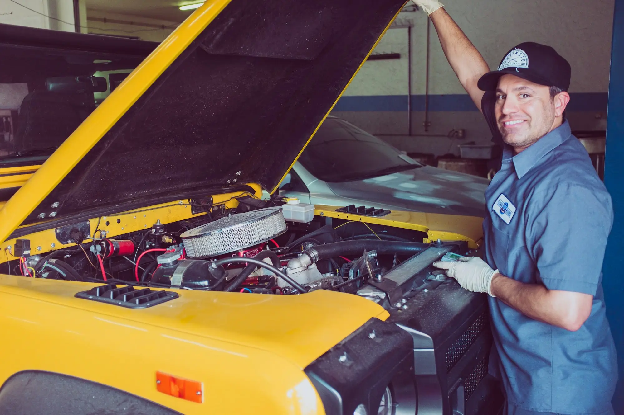 Mobile mechanic smiling while working under the bonnet of a yellow car